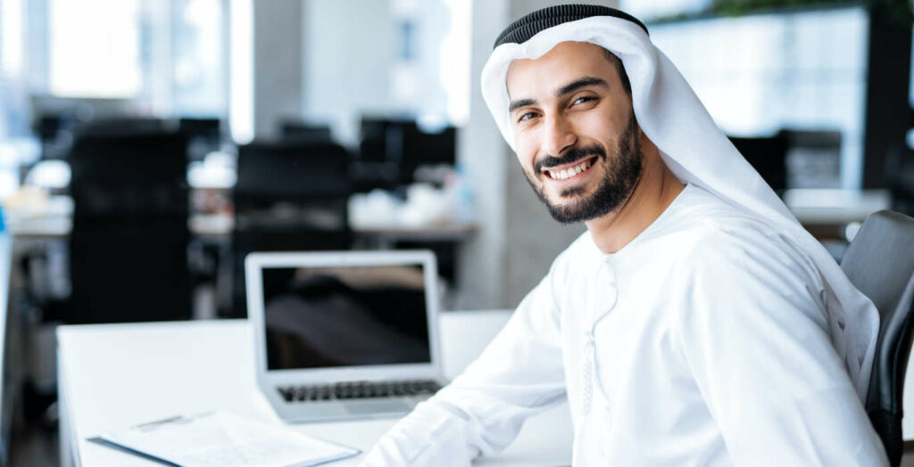Handsome man with dish dasha working in his business office of Dubai. Portraits of a successful businessman in traditional emirates white dress.